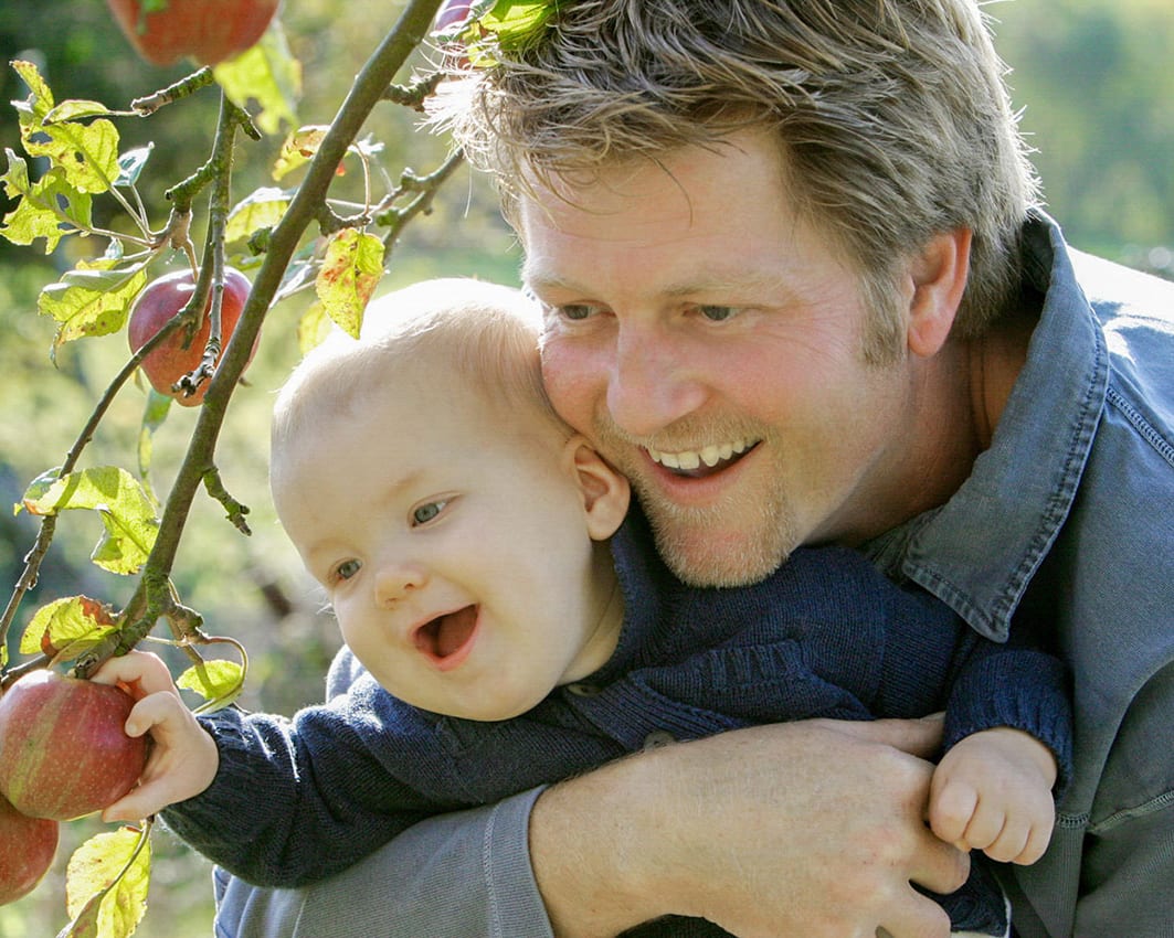 James Bignell in a portrait holding a child in an orchard